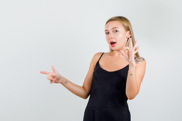 Young female pointing to side with ok sign in black singlet and looking confident 