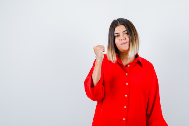 Young female pointing thumb up back in red oversized shirt and looking confident. front view.