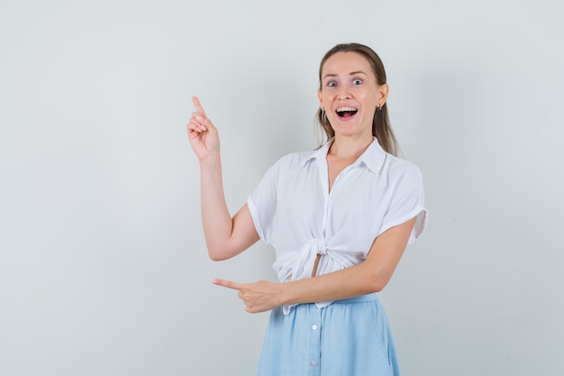 Young female pointing up in blouse, skirt and looking happy