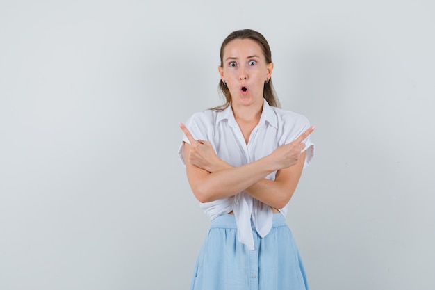 Young female pointing up in blouse, skirt and looking wondered