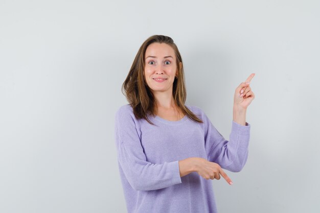 Young female pointing up and down in lilac blouse and looking hesitant 