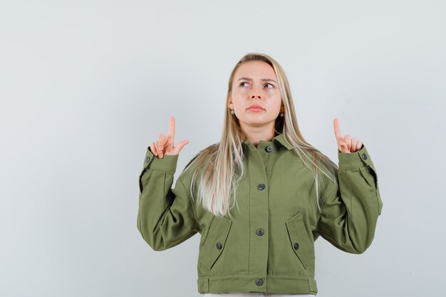 Young female pointing up in green jacket and looking confused. front view.