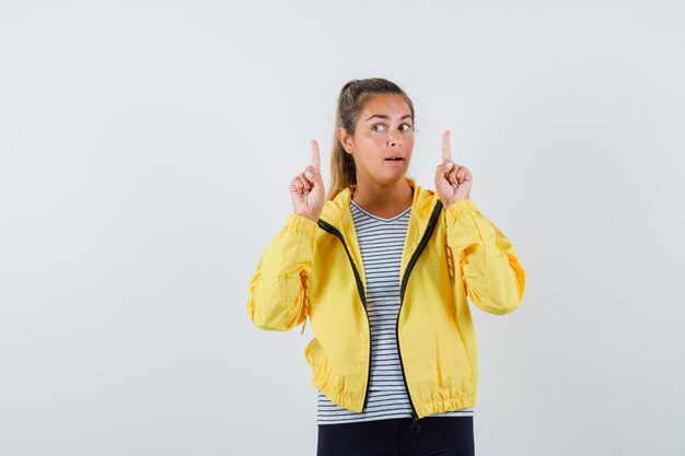 Young female pointing up in jacket, t-shirt and looking pensive. front view.