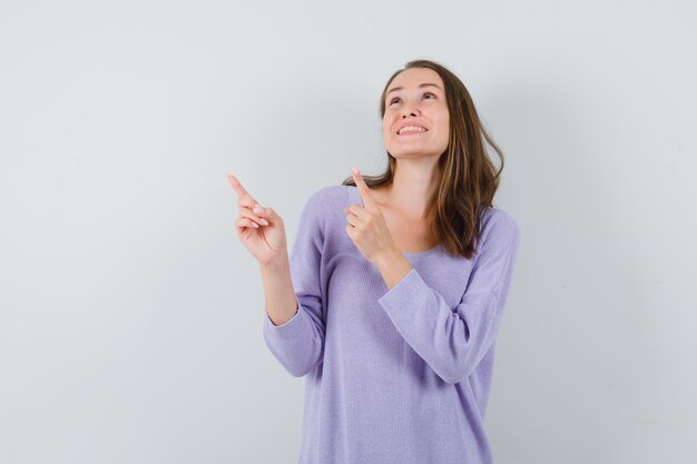 Young female pointing up in lilac blouse and looking merry 