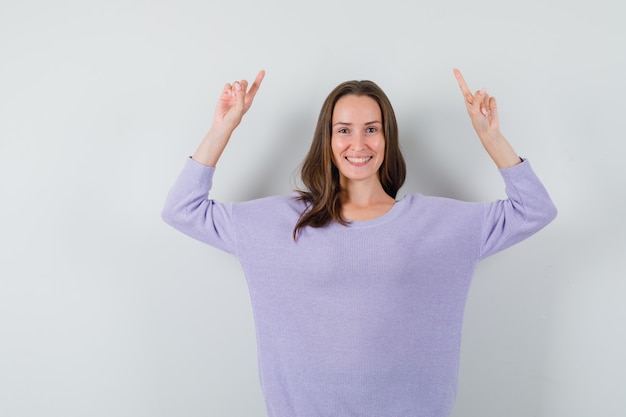 Young female pointing up while smiling in lilac blouse and looking happy 