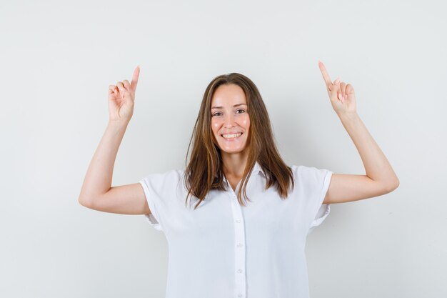 Young female pointing up in white blouse and looking cheery.