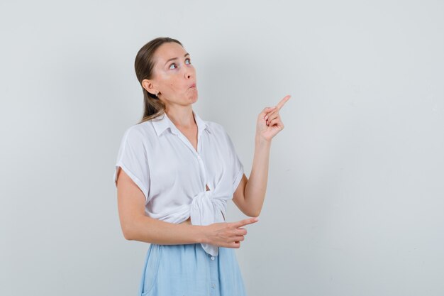 Young female pointing at upper right corner in blouse skirt and looking doubtful