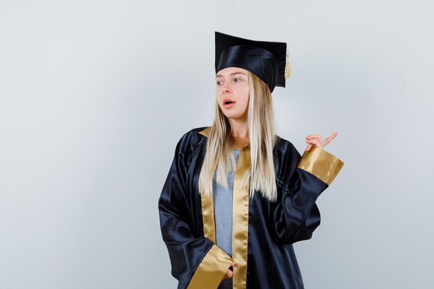 大学院の制服を着て右上を指差して物思いにふける若い女性。