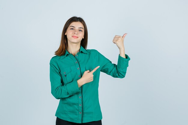 Young female pointing at upper right corner in green shirt and looking cheery , front view.