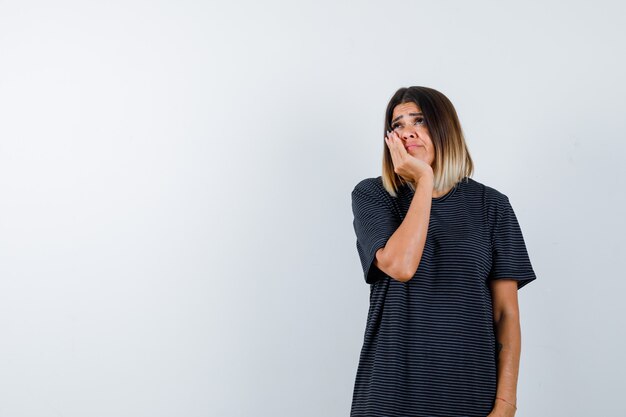 Young female in polo dress holding hand on cheek and looking cute , front view.