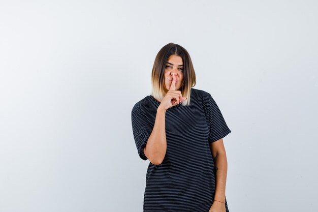 Young female in polo dress showing silence gesture and looking confident , front view.