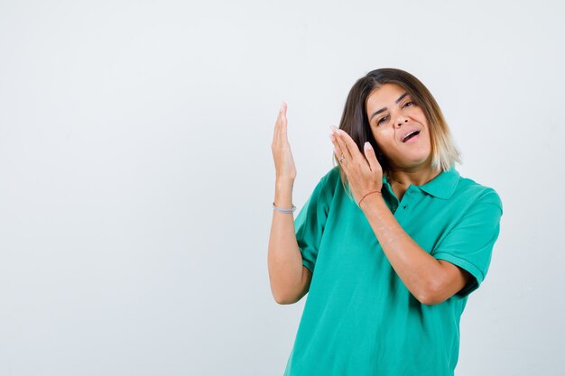 Young female in polo t-shirt showing something with palms and looking blissful , front view.