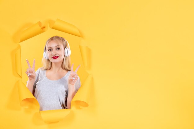 Молодая женщина позирует в наушниках на фоне порванной желтой бумаги аудио ультразвуковая музыка