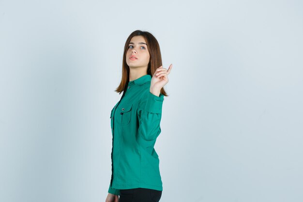 Young female posing while pointing back in green shirt and looking confident .