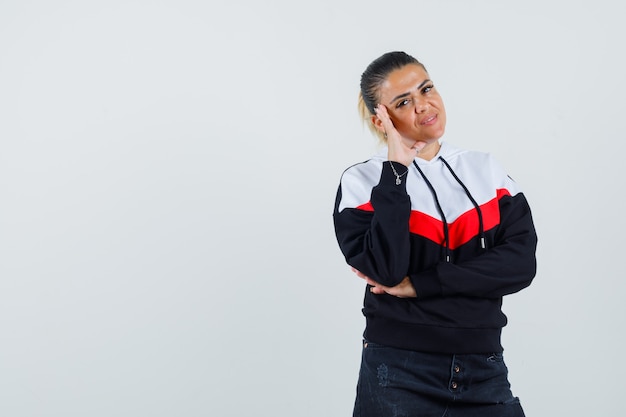 Young female posing with hand on head in colorful sweatshirt , front view. 