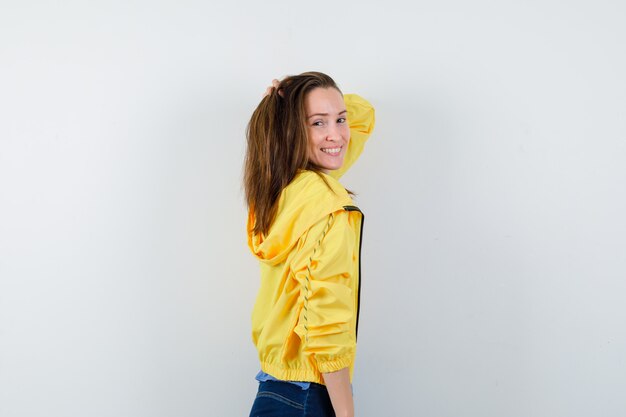 Young female posing with hand on head in yellow jacket and looking alluring.