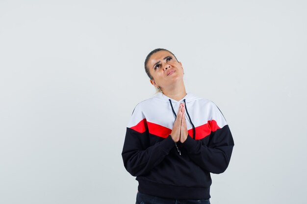 Young female praying in colorful sweatshirt and looking hopeful. front view.