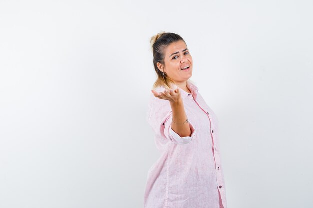 Young female pretending to offer something in pink shirt and looking merry 