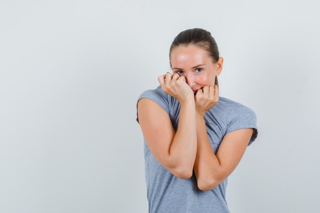 Young female pulling collar on face in grey t-shirt and looking shy , front view.