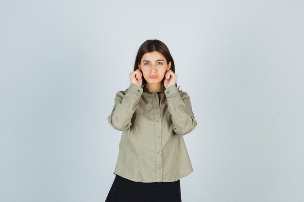 Young female pulling down her earlobes, curving lower lip in shirt