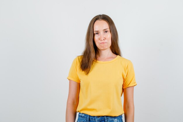 Молодая женщина сжимает губы в футболке, шортах и выглядит грустной