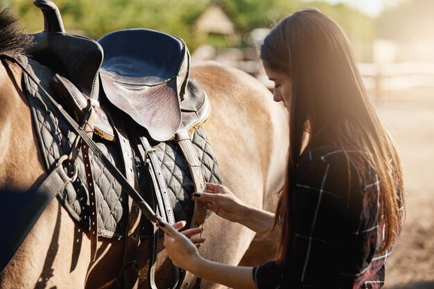 若い女性の競走馬の調教師がサドルを準備してロックダウン