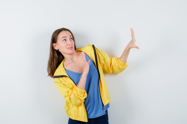 Young female raising hands to defend herself in t-shirt, jacket and looking scared, front view.