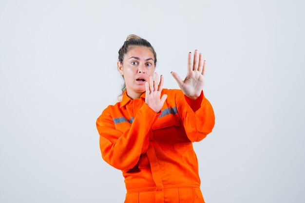 Giovane donna alzando le mani per difendere in uniforme da lavoro e guardando turbato. vista frontale.