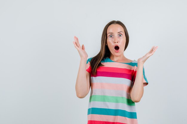 Young female raising hands in t-shirt and looking scared. front view.