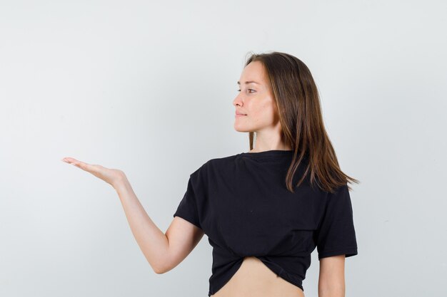 Young female raising palm like holding something in black blouse and looking confident