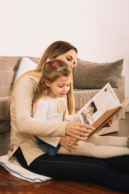 Young female reading book with daughter on floor