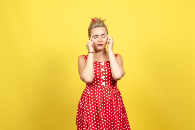 young female in red polka dot dress closing her eyes on yellow