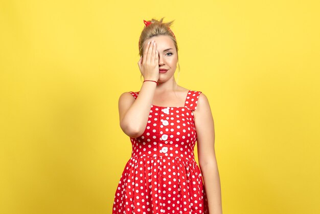 young female in red polka dot dress covering half of her face on yellow