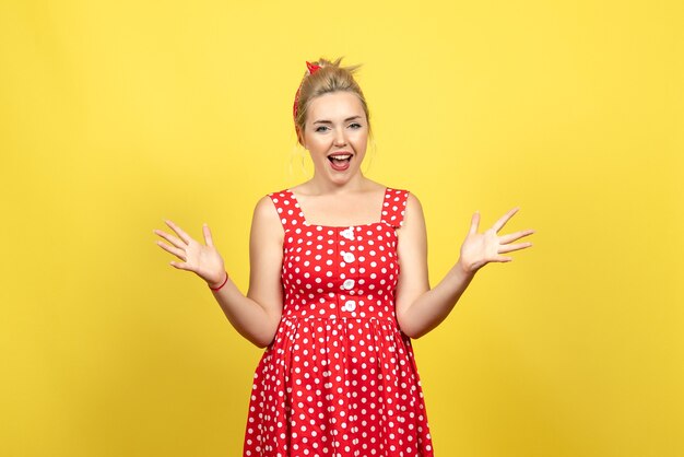 young female in red polka dot dress emotionally posing on yellow