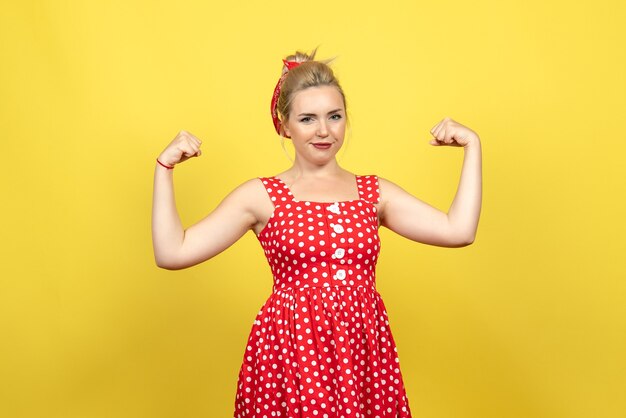 young female in red polka dot dress flexing on yellow