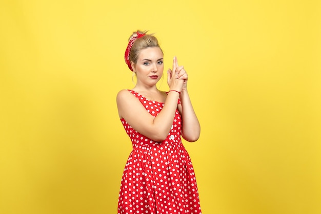 young female in red polka dot dress and gun holding pose on yellow