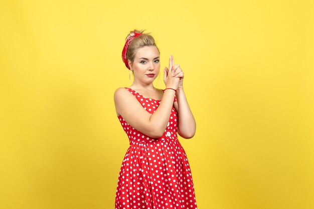 young female in red polka dot dress and gun holding pose on yellow