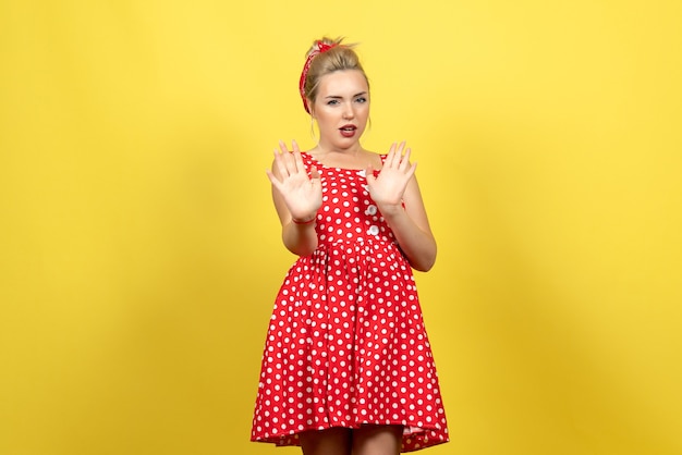 ちょうど黄色の上に立っている赤い水玉模様のドレスの若い女性