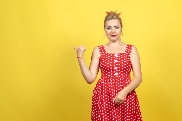 young female in red polka dot dress pointing aside on yellow