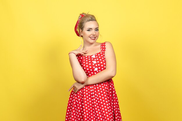 young female in red polka dot dress posing on light yellow