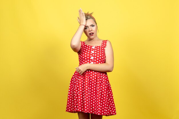 young female in red polka dot dress posing on light yellow