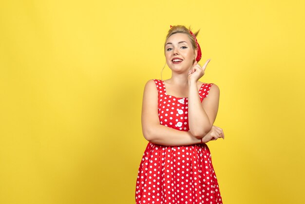 young female in red polka dot dress posing on light yellow