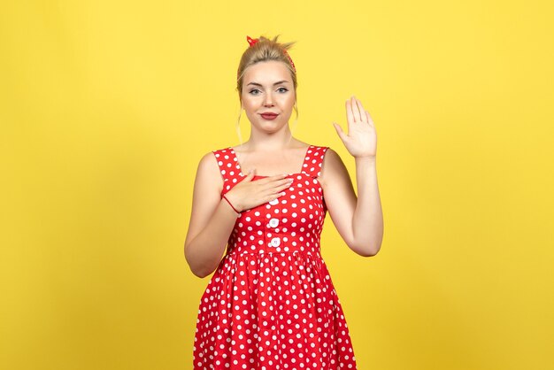 young female in red polka dot dress posing raising her hand on yellow