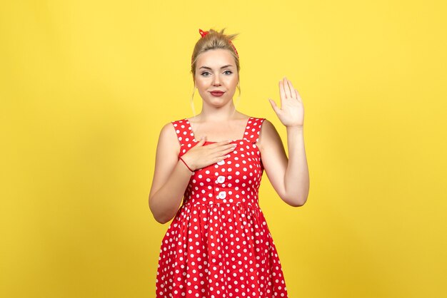 молодая женщина в красном платье в горошек позирует, поднимая руку на желтом