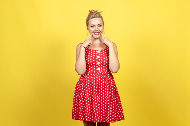 young female in red polka dot dress posing and smiling on yellow