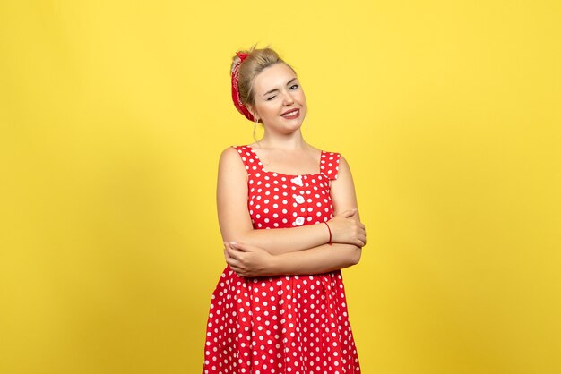 young female in red polka dot dress posing and winking on yellow