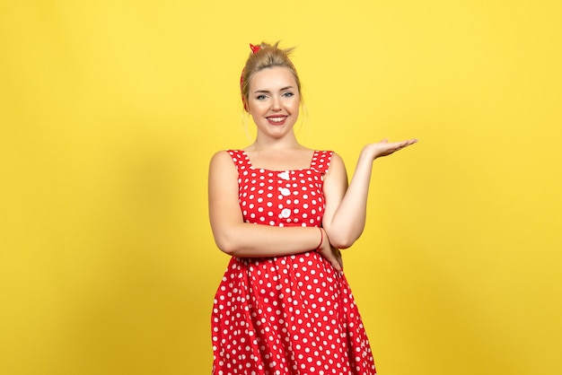 Free photo young female in red polka dot dress posing with smile on yellow