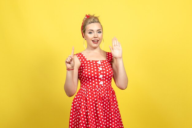 young female in red polka dot dress posing on yellow