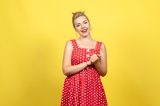 young female in red polka dot dress posing on yellow