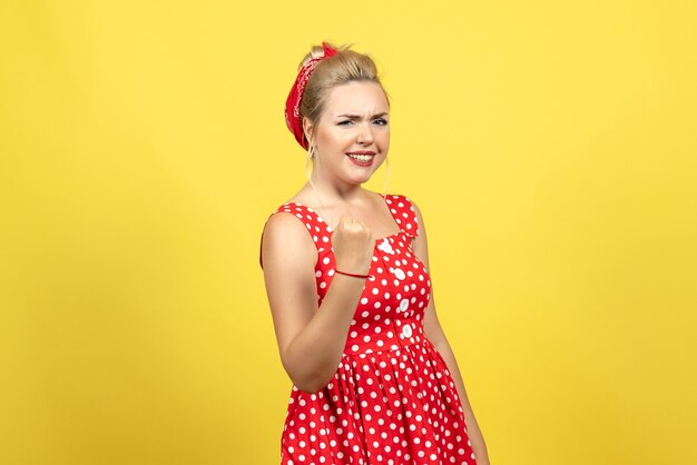 young female in red polka dot dress posing on yellow